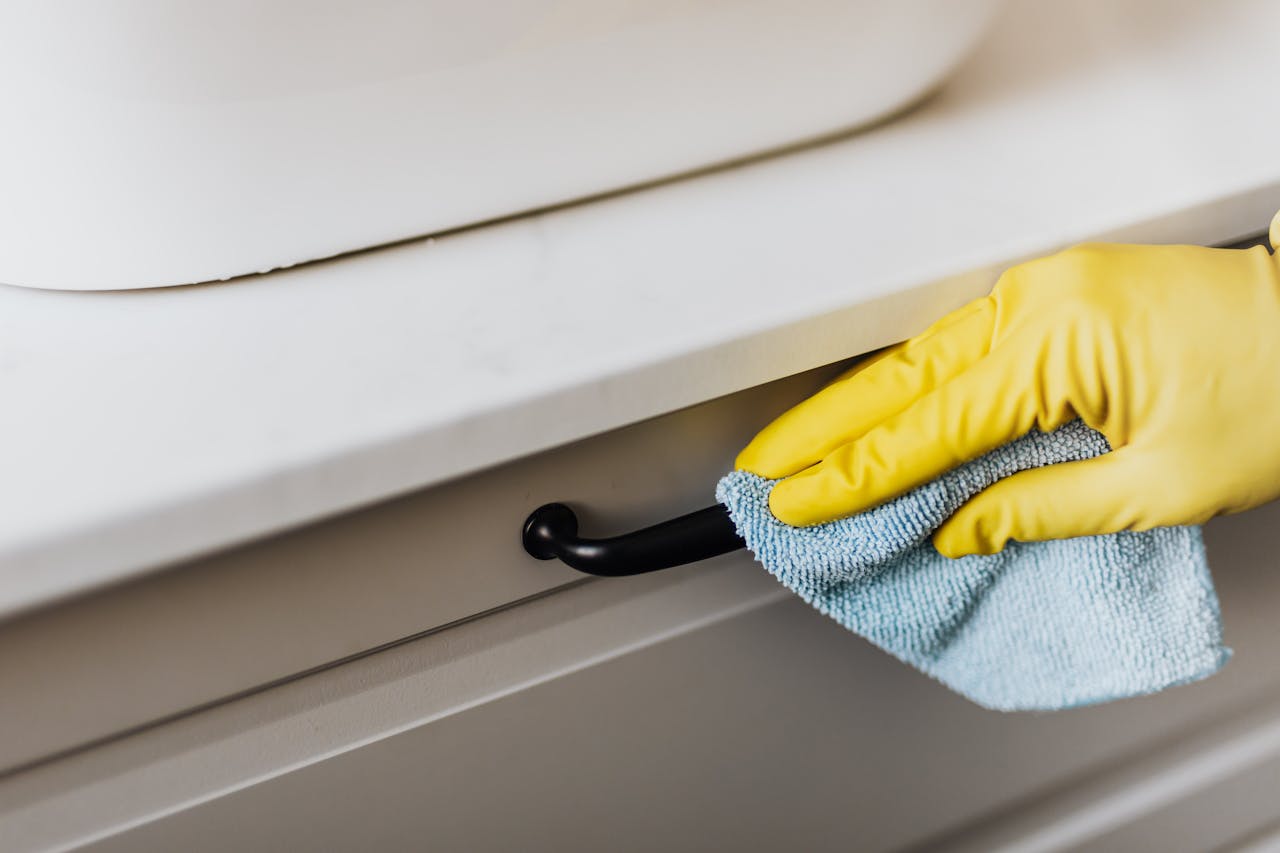 Home From above of crop faceless person in yellow gloves cleaning handle of cabinet with microfiber cloth in modern bright bathroom