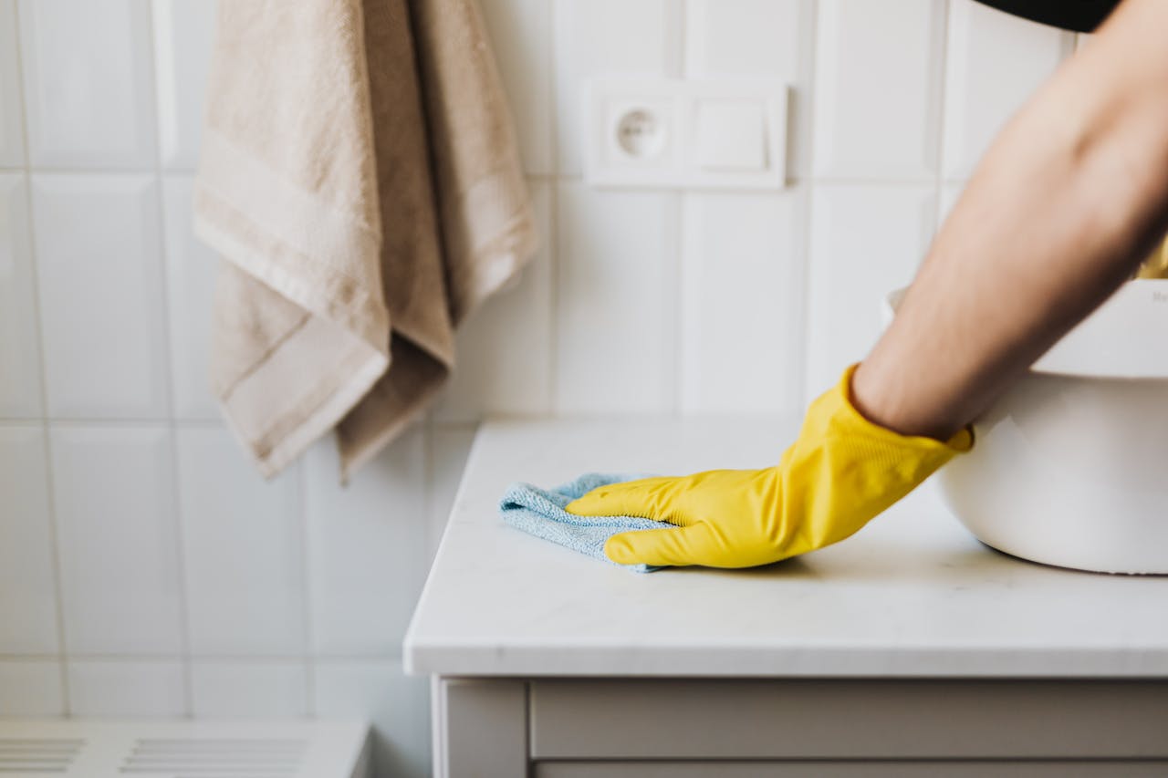 Home Close-up of a person wearing yellow gloves wiping a bathroom counter with a cloth.