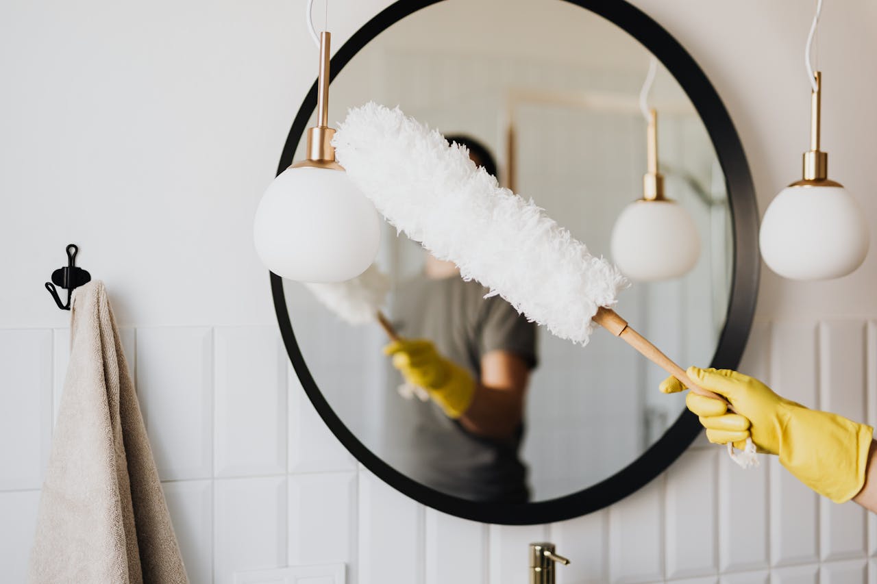 Home A person cleaning an elegant bathroom mirror with a fluffy duster and yellow gloves.